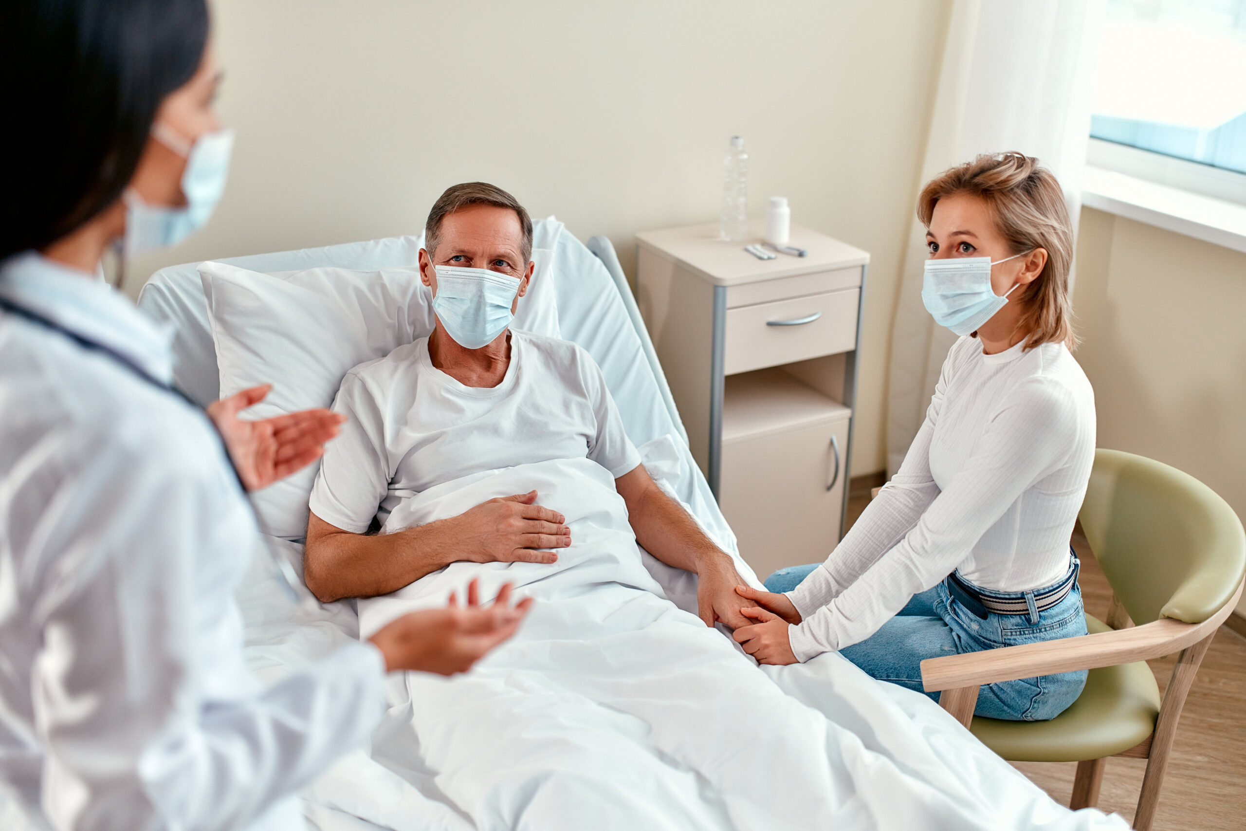 A beautiful woman doctor in a protective medical mask communicates with the family of a mature patient who is lying in a modern hospital ward during the coronavirus or covid-19 epidemic. Personal Injury Lawyer assisting with filing a claim on someone else's behalf.