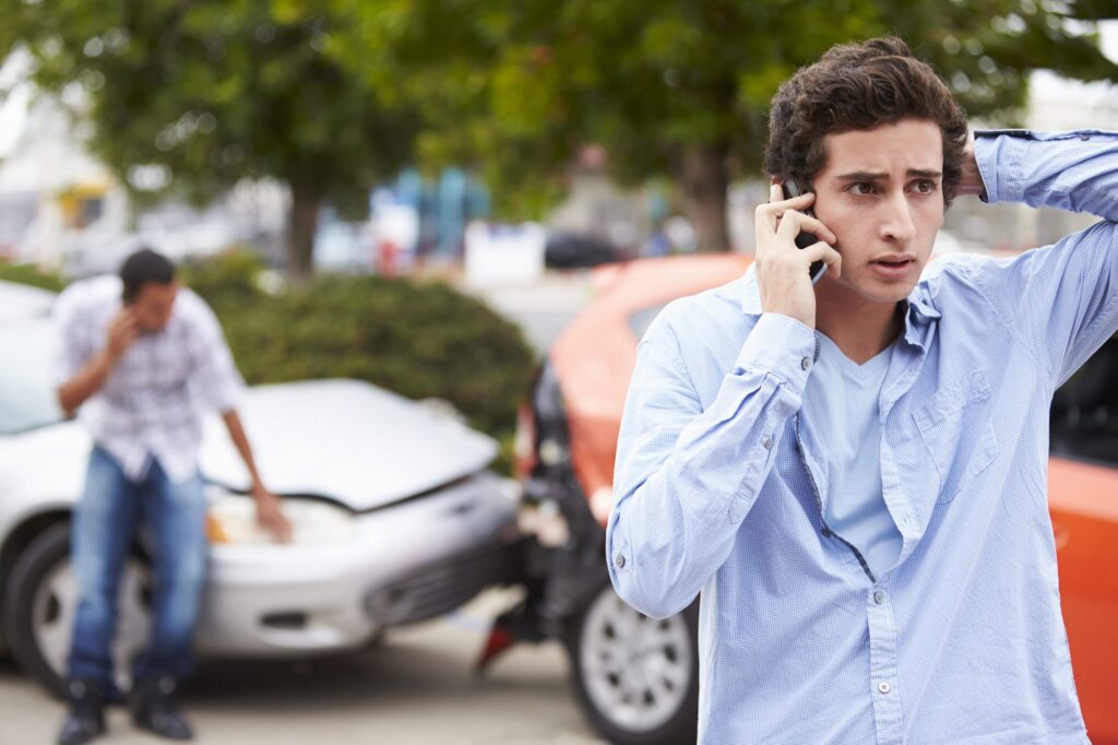 Young man on the phone after a minor fender bender, reporting the crash — should I get a lawyer for a minor car accident?