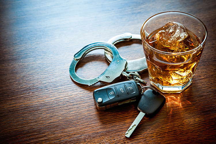 Car keys and handcuffs beside a glass of whiskey on a wood table, symbolizing DUI arrests and open-container laws. Can you drink non-alcoholic beer while driving? 