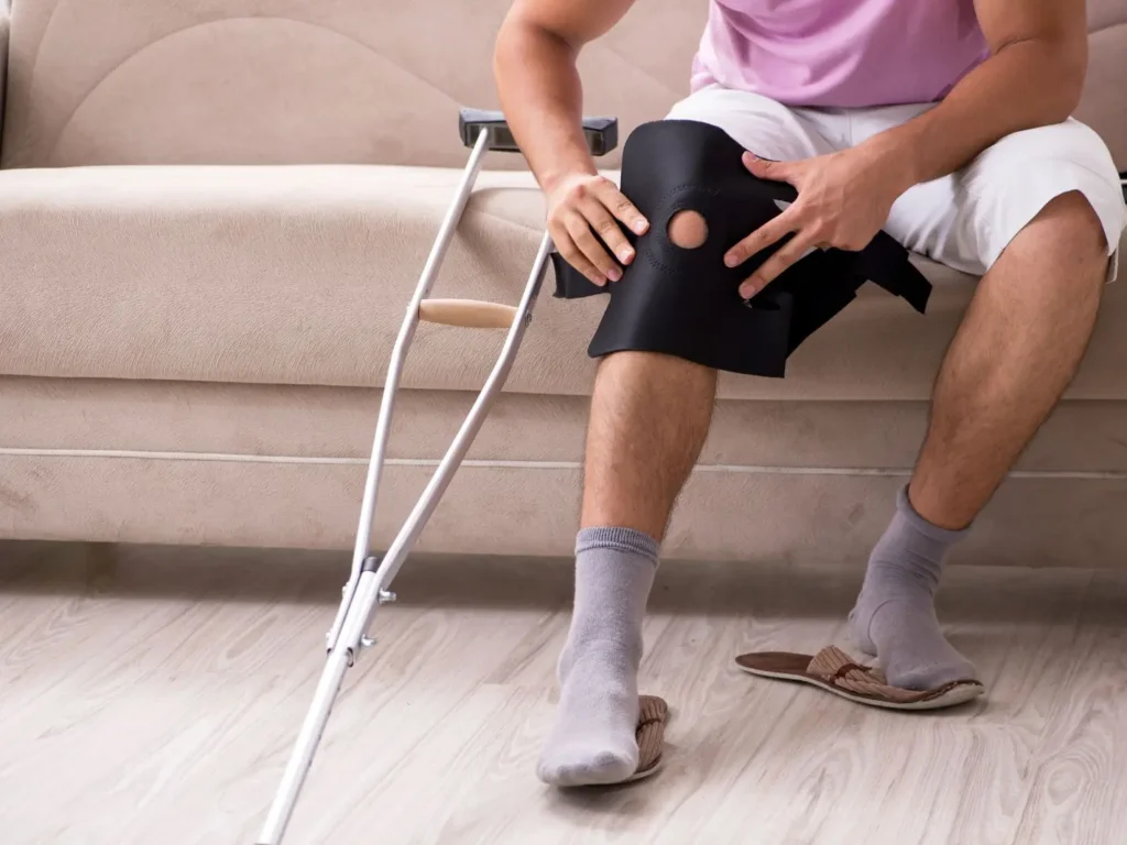 Injured man with crutches and a knee brace sitting on a couch, representing how trusted personal injury lawyers at Thompson Law help injury victims recover compensation.